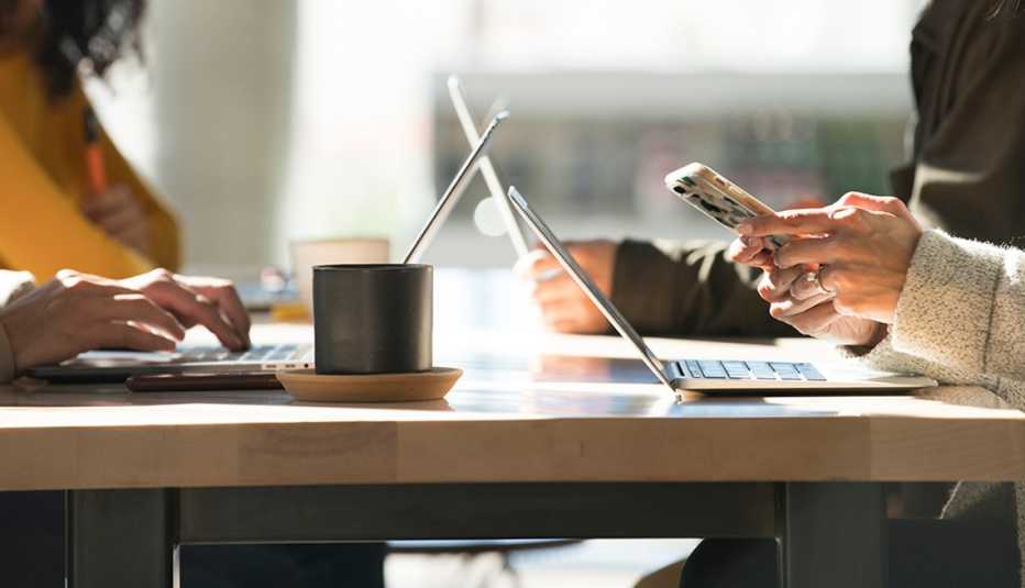 Dos personas con sus computadoras y sus teléfonos sobre una mesa.