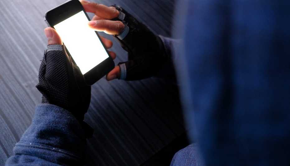 Persona con sueter de capucha y guantes observa un teléfono móvil.
