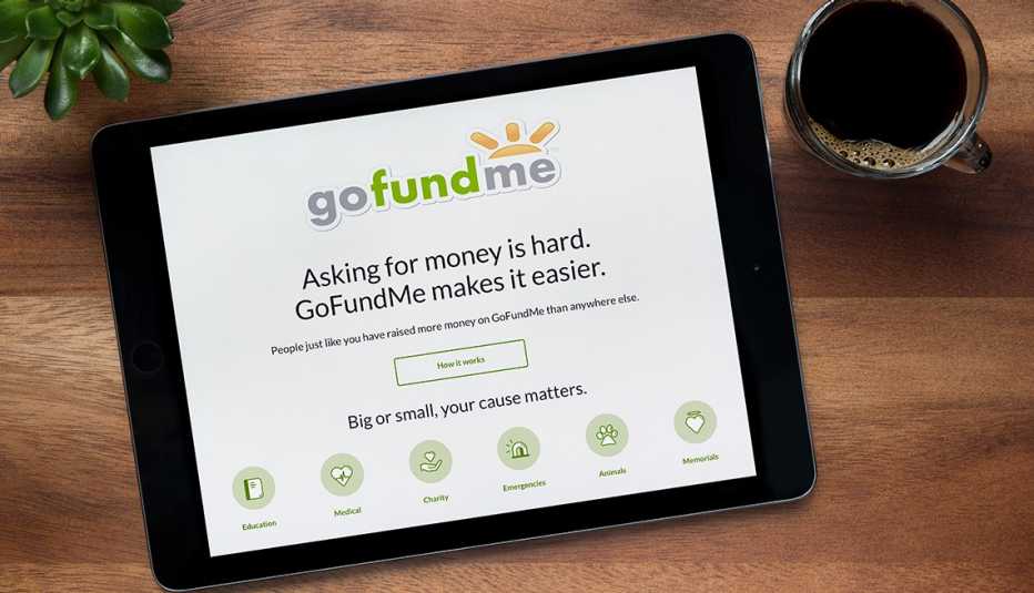 Tableta que muestra el sitio web GoFundMe sobre una mesa de madera, al lado de una taza de café y una planta