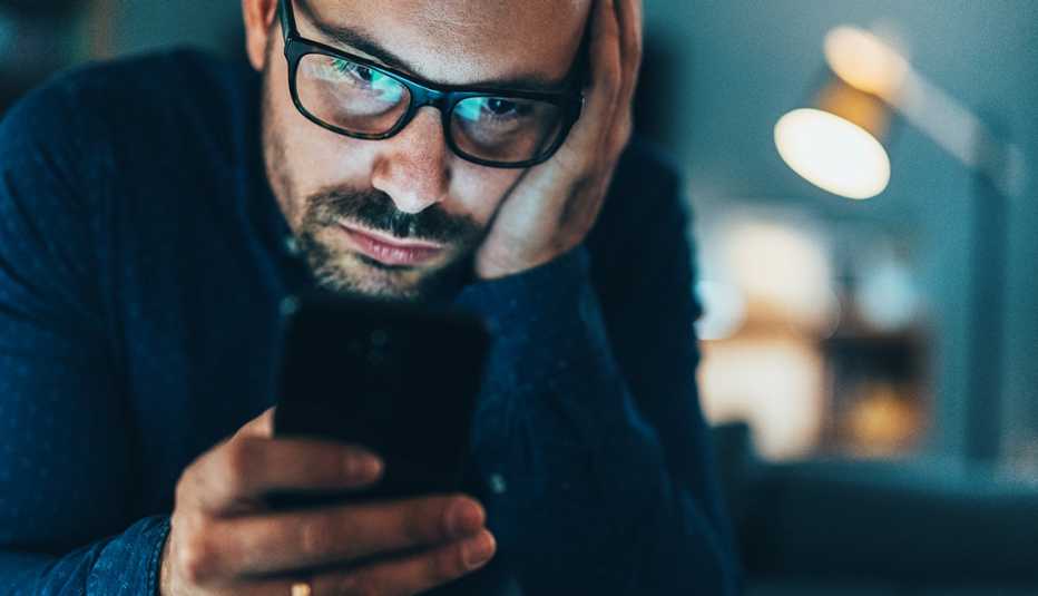 Hombre viendo su teléfono móvil el cual sostiene en su mano.