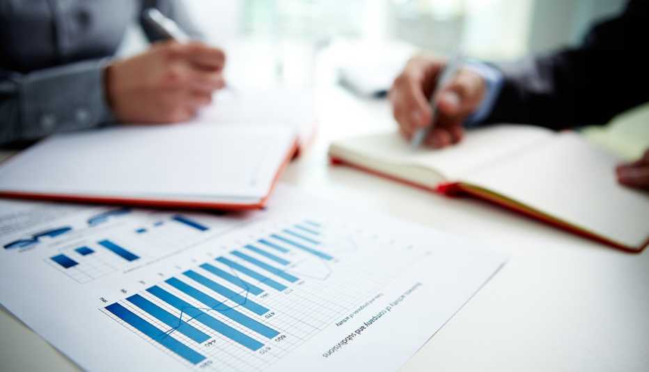Manos de dos hombres tomando notas de una gráfica estadística