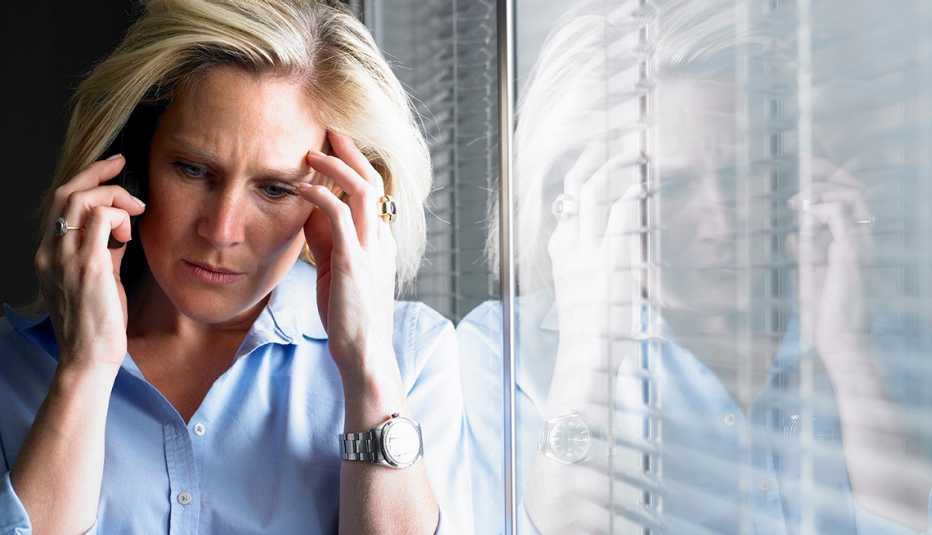 Mujer apoyándose en una ventana y con cara de preocupación
