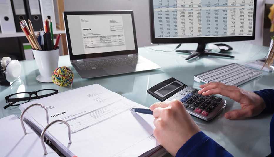 Persona haciendo cuentas en su oficina con facturas, computadora, calculadora, libreta y lapiceros. Persona haciendo cuentas en su oficina con facturas, computadora, calculadora, libreta y lapiceros.