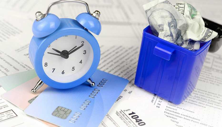 Formularios 1040 del IRS debajo de un reloj despertador y al lado de cubo con dólares. Formularios 1040 del IRS debajo de un reloj despertador y al lado de cubo con dólares.
