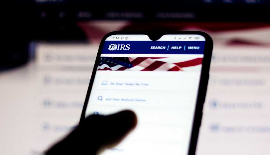 Persona sosteniendo un teléfono móvil con la página del IRS en la pantalla.