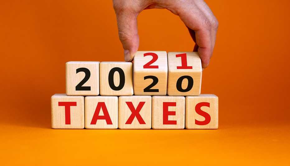 Mano cambiando al año 2021 en unos cubos de madera apoyados en otros que dicen impuestos.