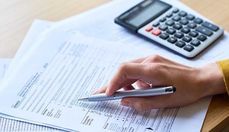 Manos de una persona sobre formularios del IRS al lado de una calculadora.