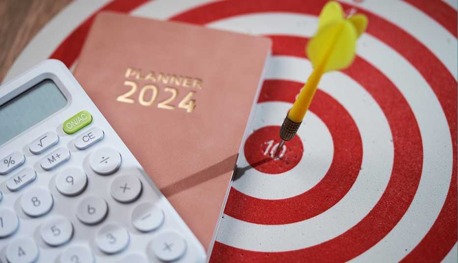 Un dardo ha dado en el blanco en un tablero de dardos, junto a un libro de agenda de planificación para 2024 y una calculadora