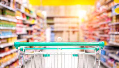 Un carrito de supermercado visto desde una perspectiva baja con los estantes del pasillo y los artículos borrosos