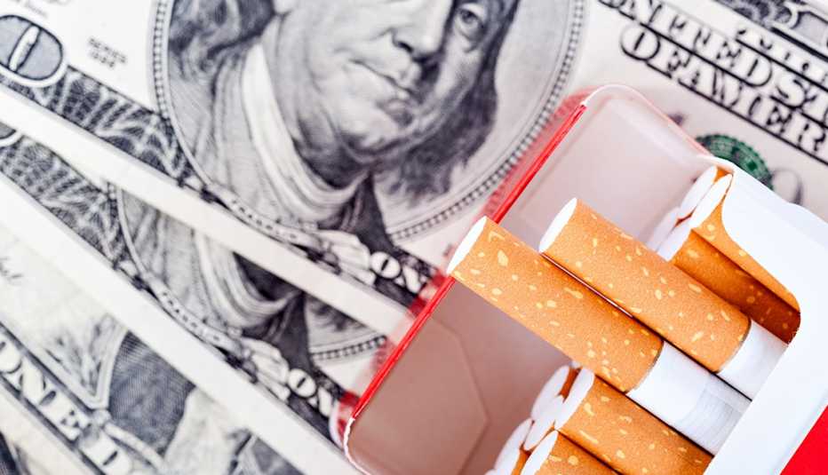 Caja de cigarrillos abierta y billetes de 100 dólares al fondo. Caja de cigarrillos abierta y billetes de 100 dólares al fondo.