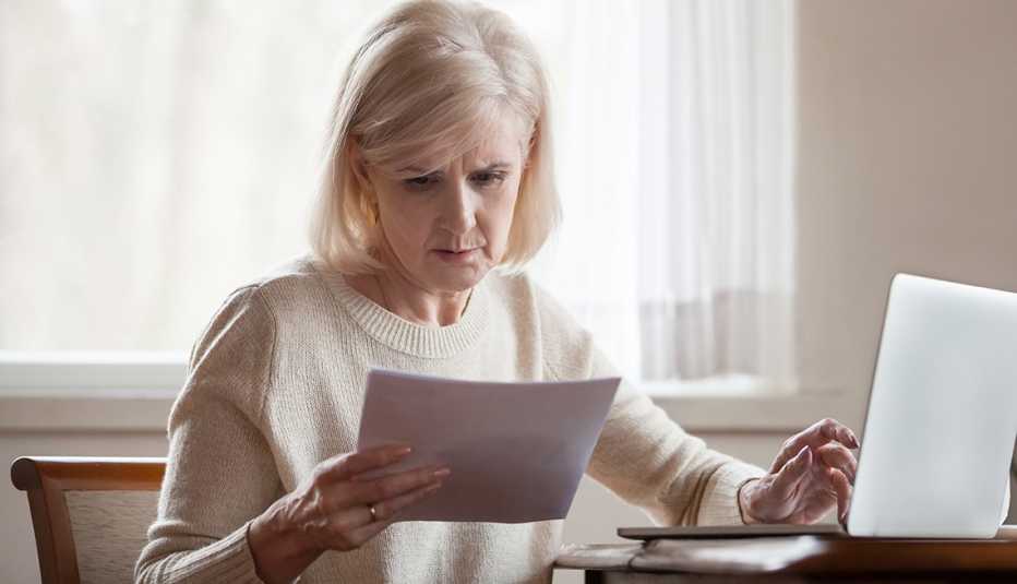 Mujer sosteniendo facturas en una mano y con la otra en la computadora.