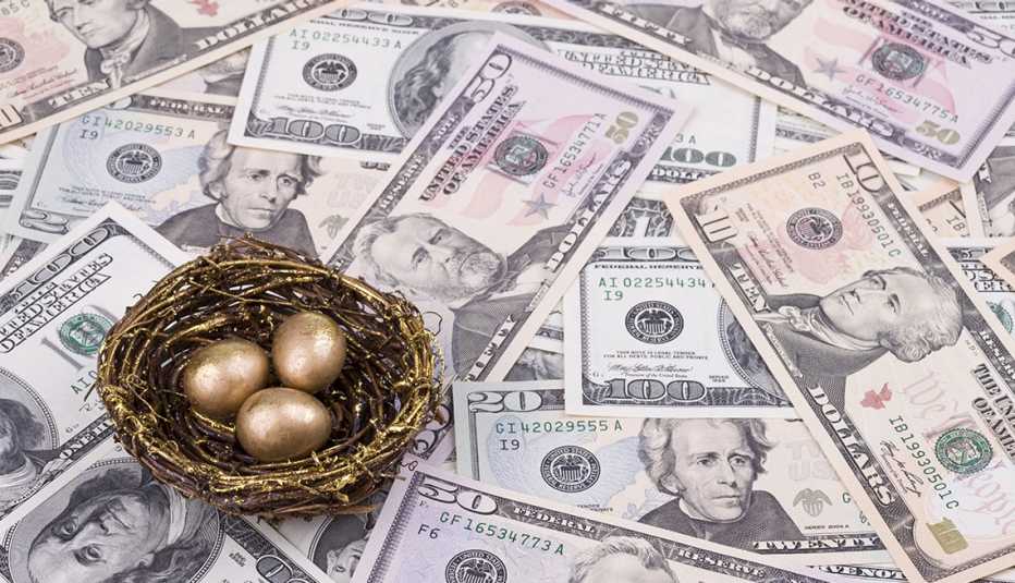 Nido con huevos de oro encima de una superficie llena de dólares.