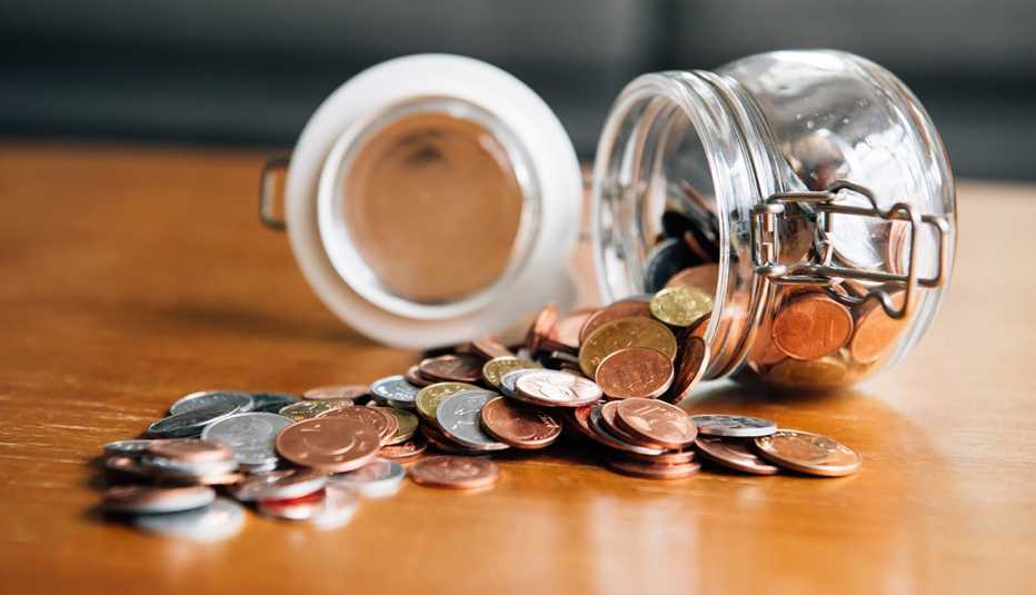 Jarra de lado con la tapa abierta sobre una mesa donde caen las monedas.