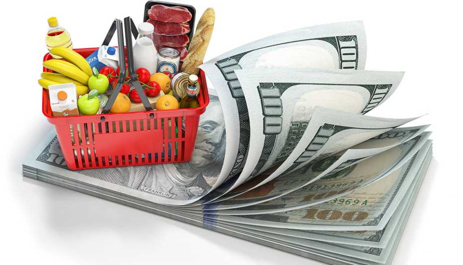 Canasta llena de frutas, verduras y embutidos sobre un fajo de billetes de 100 dólares
