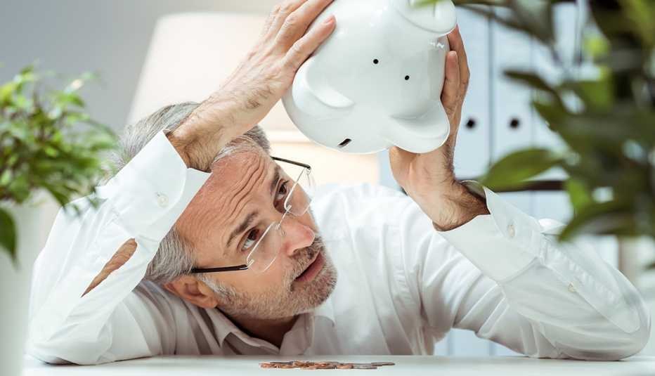 Hombre sosteniendo una alcancía bocabajo para sacar las monedas.