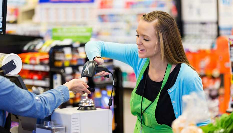 Cajera en un supermercado registra un cupón que una persona enseña desde la pantalla de su teléfono. Cajera en un supermercado registra un cupón que una persona enseña desde la pantalla de su teléfono.