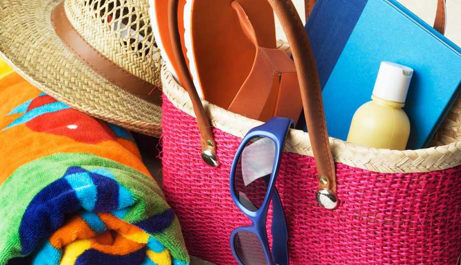 Bolso de verano con un protector solar, una libreta, unas gafas de sol, un sombrero, una toalla y unas sandalias