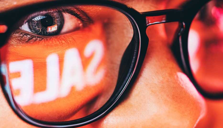 Primer plano de una mujer comprando en una computadora con la palabra "OFERTA" reflejada en sus anteojos.