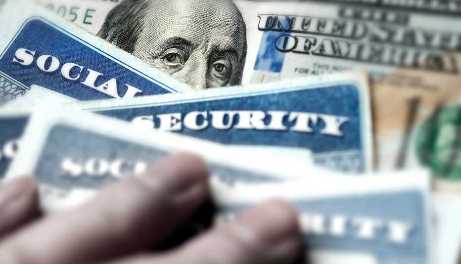 Mano sobre varias tarjetas del Seguro Social y billetes de 100 dólares Mano sobre varias tarjetas del Seguro Social y billetes de 100 dólares