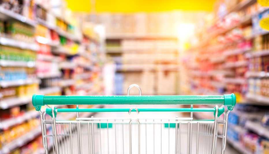 Un carrito de supermercado visto desde una perspectiva baja con los estantes del pasillo y los artículos borrosos
