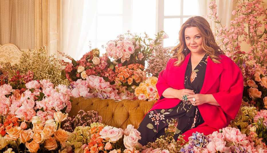 Melissa McCarthy sentada en medio de arreglos florales