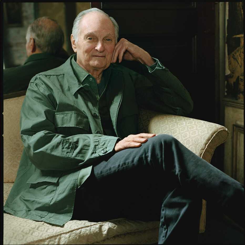Actor Alan Alda sentado en un sofá y con un espejo al fondo.