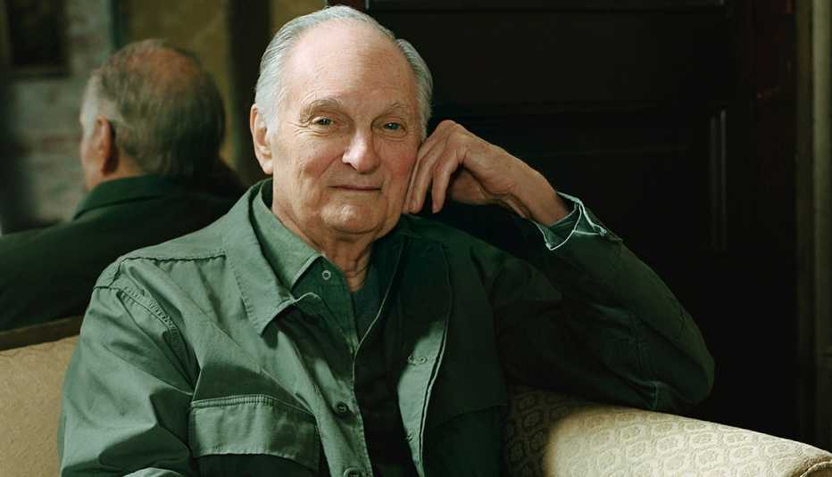Alan Alda sentado en un sofá con un espejo en el fondo.