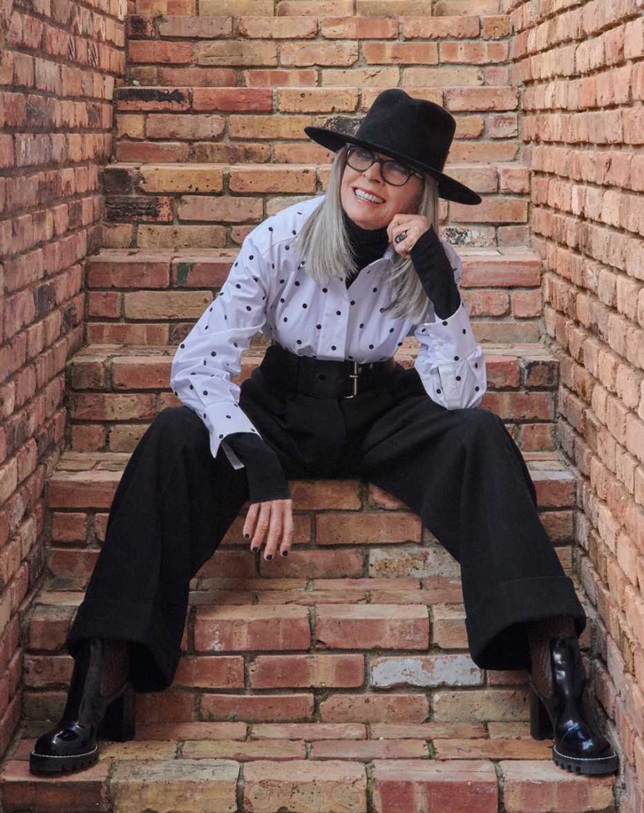Diane Keaton sentada en unas escaleras usando uno de sus famosos sombreros.