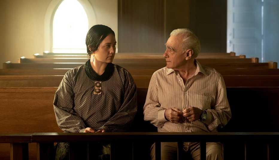 Lily Gladstone y Martin Scorcese mientras filman “Killers of the Flower Moon". lily gladstone and director martin scorsese sitting next to each other in a chapel in a scene from the film killers of the flower moon