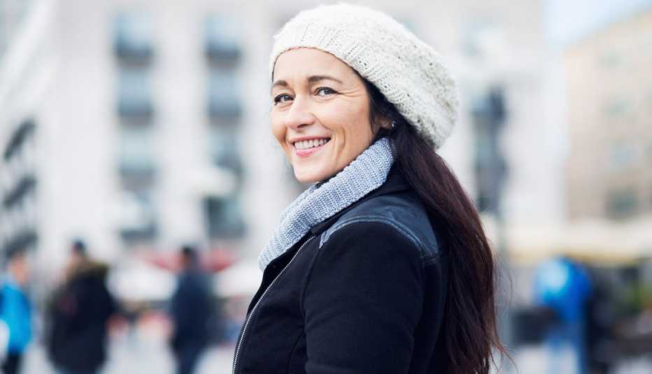 Mujer vestida con ropa de invierno y sonriendo porque cuida su piel en este temporada