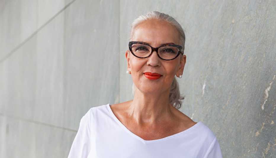 Mujer mayor con lentes, pelo recogido de color gris, sonríe.