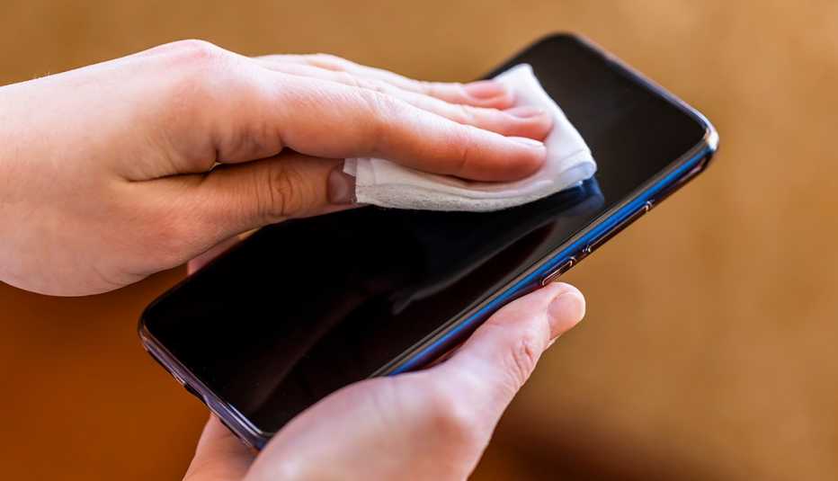 Manos de una mujer limpiando un teléfono móvil con un paño.