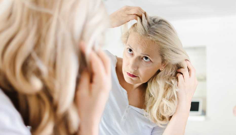 Mujer mirando su cabello frente a un espejo.