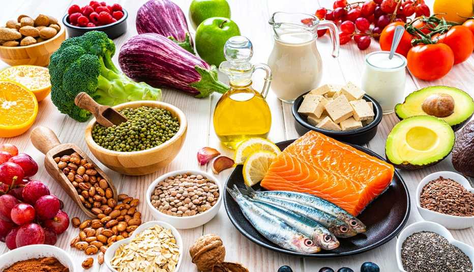 Una variedad de alimentos mostrados en una mesa que incluyen frijoles, pescado, frutas, verduras, leche y aceite de oliva.