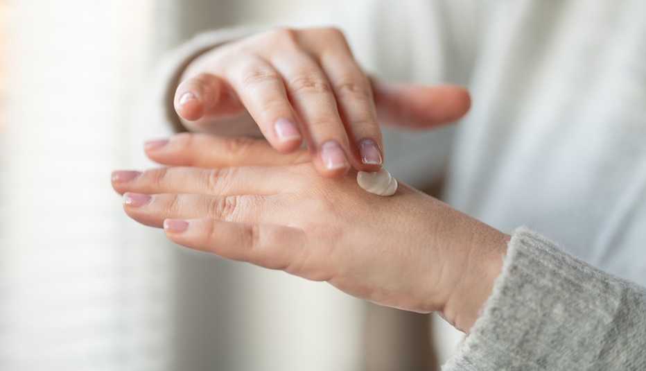 Mujer aplicándose crema en las manos.