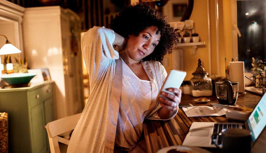 Mujer usando su teléfono y computadora en casa.