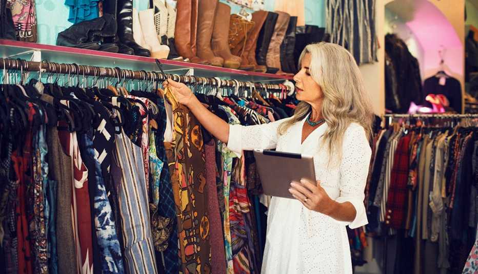 Mujer usando una tableta mientras sostiene un vestido en la tienda.