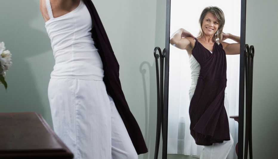 Una mujer sosteniendo un vestido negro frente a su cuerpo y mirándose en un espejo.