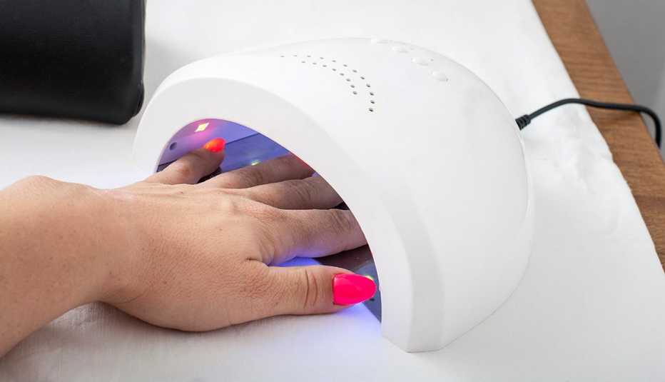 Una mano con manicura dentro de un secador de esmalte. Una mano con manicura dentro de un secador de esmalte.