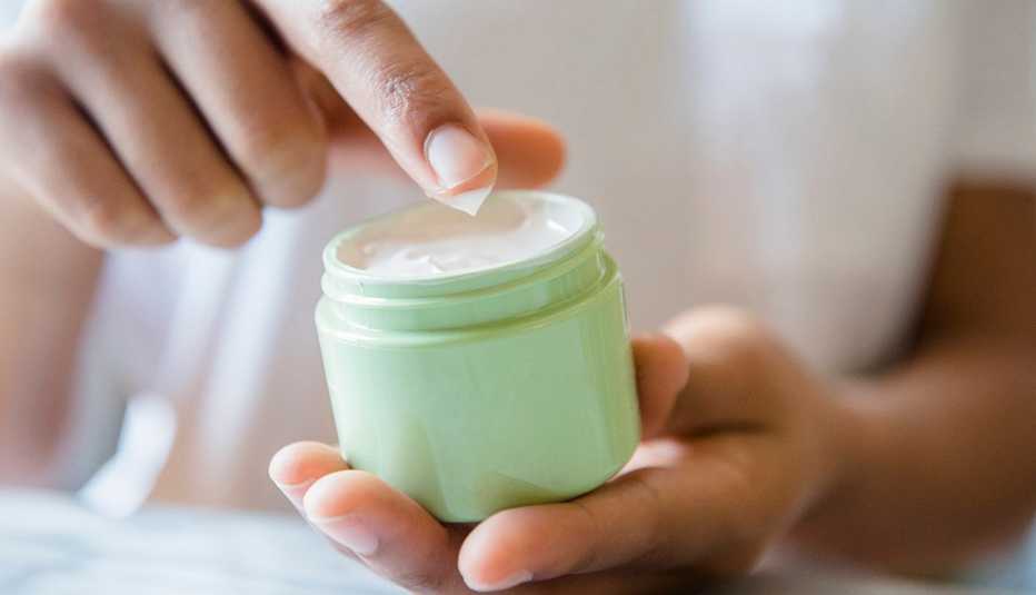 Una mujer sostiene un envase de crema en sus manos.