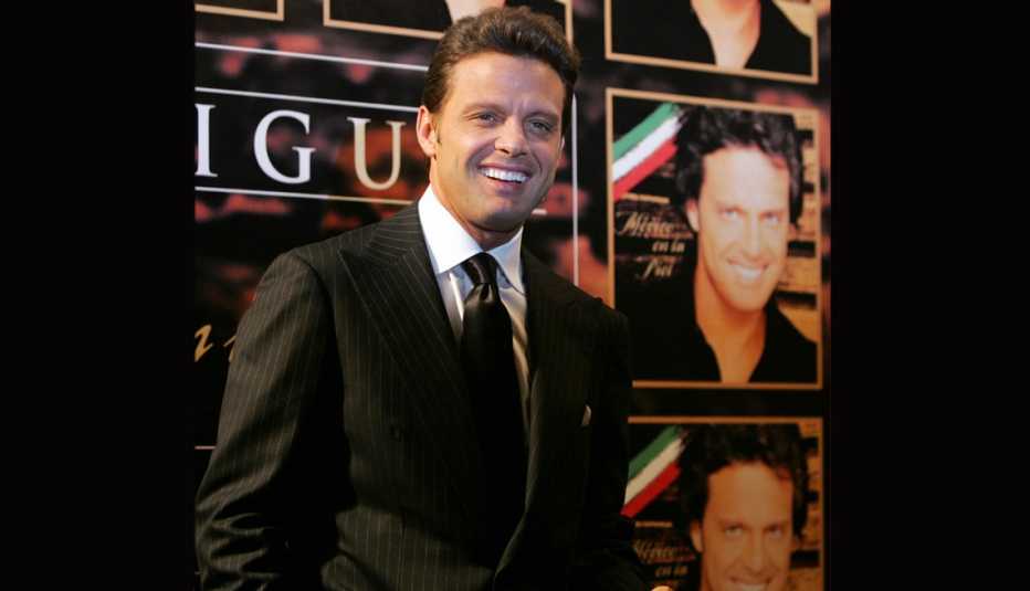 Luis Miguel sonriendo frente una pared con la portada de su disco