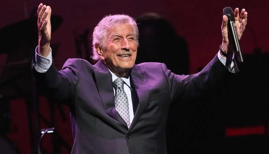 Tony Bennett levanta los brazos en el aire durante una actuación en el escenario.