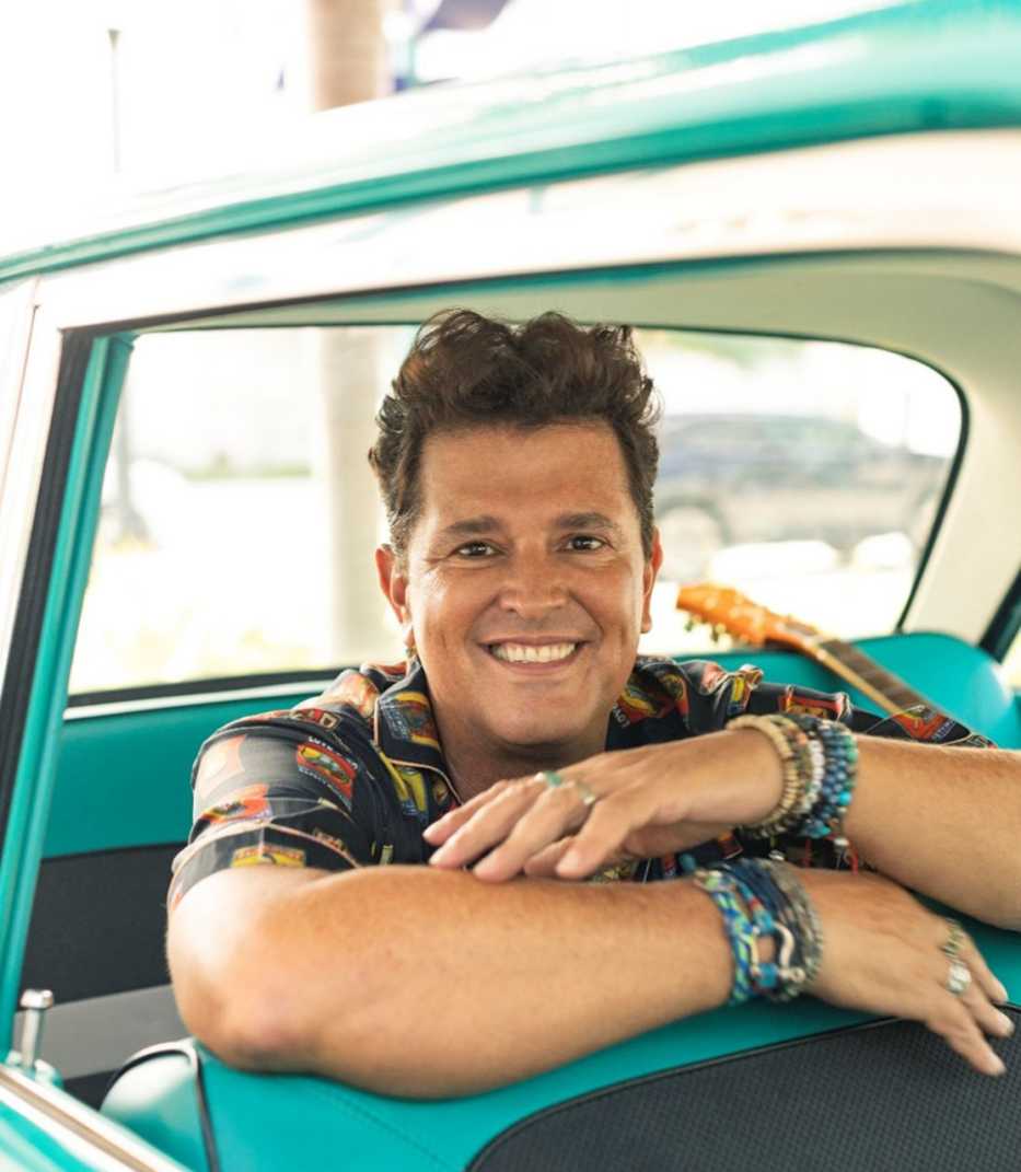 Carlos Vives sonríe sentado dentro de un auto clásico. Carlos Vives.