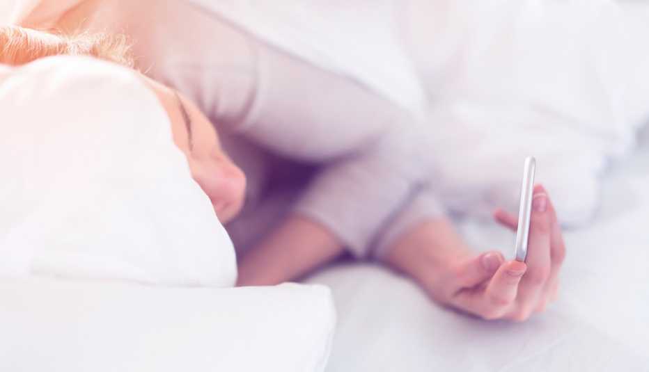 Mujer adulta ve su teléfono mientras está en la cama