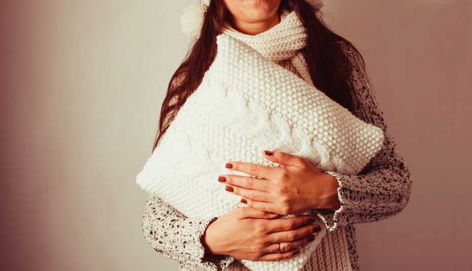 Mujer vestida con un saco de lana sostiene un cojín blanco tejido