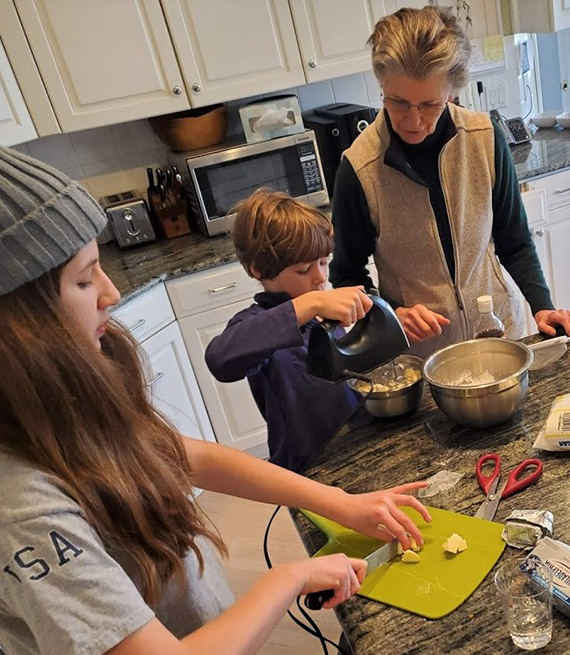 Abuela con sus nietos en una mesa de cocina mezclando masa para torta
