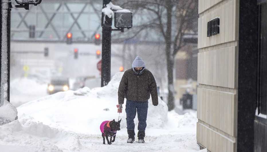 Un hombre pasea a su perro por la acera durante una tormenta de nieve en Iowa. a man walks his dog along the sidewalk during a snowstorm in Iowa