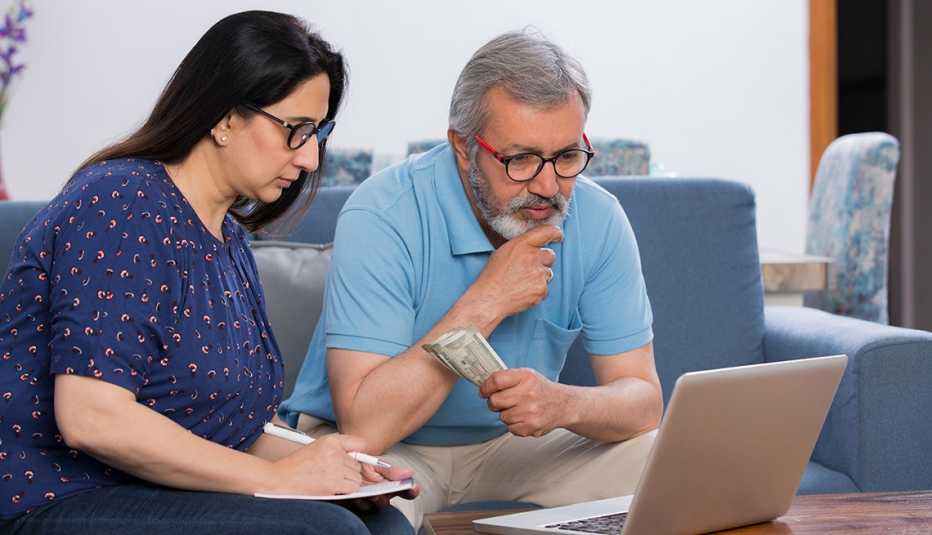 Pareja mayor haciendo cuentas frente a una computadora portátil en la sala de su casa.