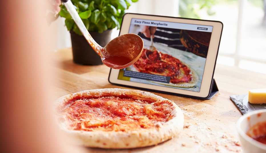 Persona parcialmente fuera de cámara vierte salsa sobre la masa de pizza 