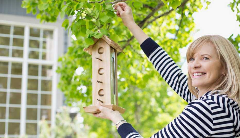 A woman smiles as she fills a bird house in a yard.